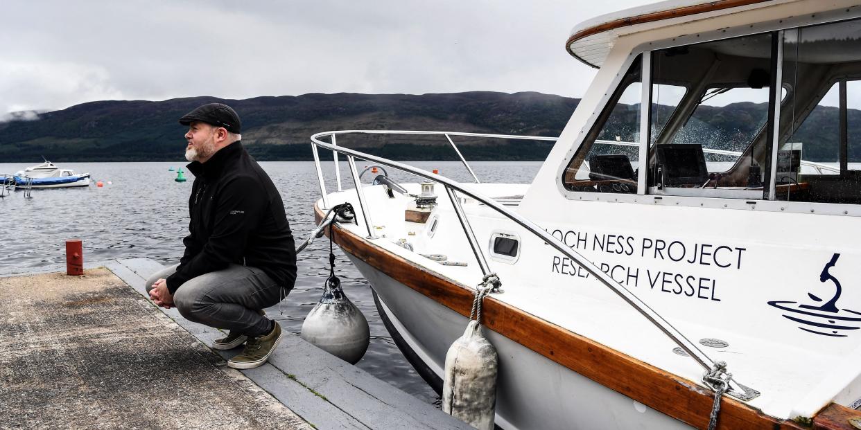 Alan McKenna, organiser of the Loch Ness Monster Hunt, squats on a pier on the shores of Loch Ness on August 27, 2023.