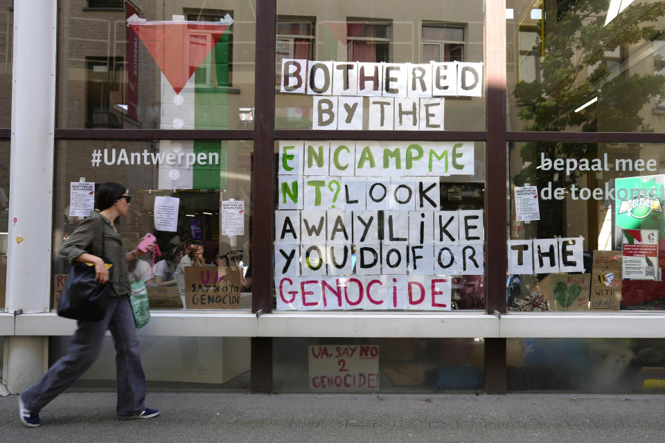 A woman walks by signs hanging in a window inside of a school building at the University of Antwerp, as pro-Palestinian students occupy parts of the campus in Antwerp, Belgium, Tuesday, May 14, 2024. (AP Photo/Virginia Mayo)