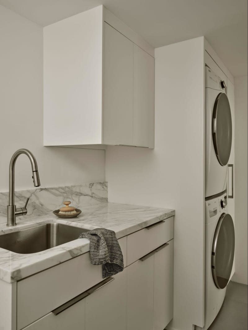 White cabinets, stacked washer and dryer, gray marble counter top with laundry sink