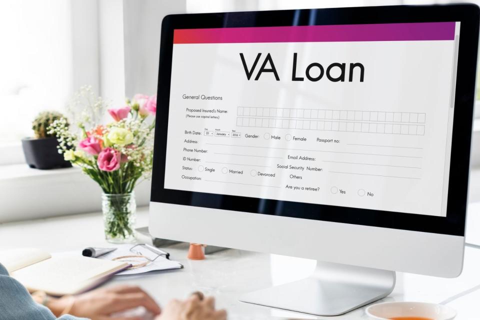 A close up of a desktop's showing 'VA Loan' on the screen and flowers in a vase on the desk.