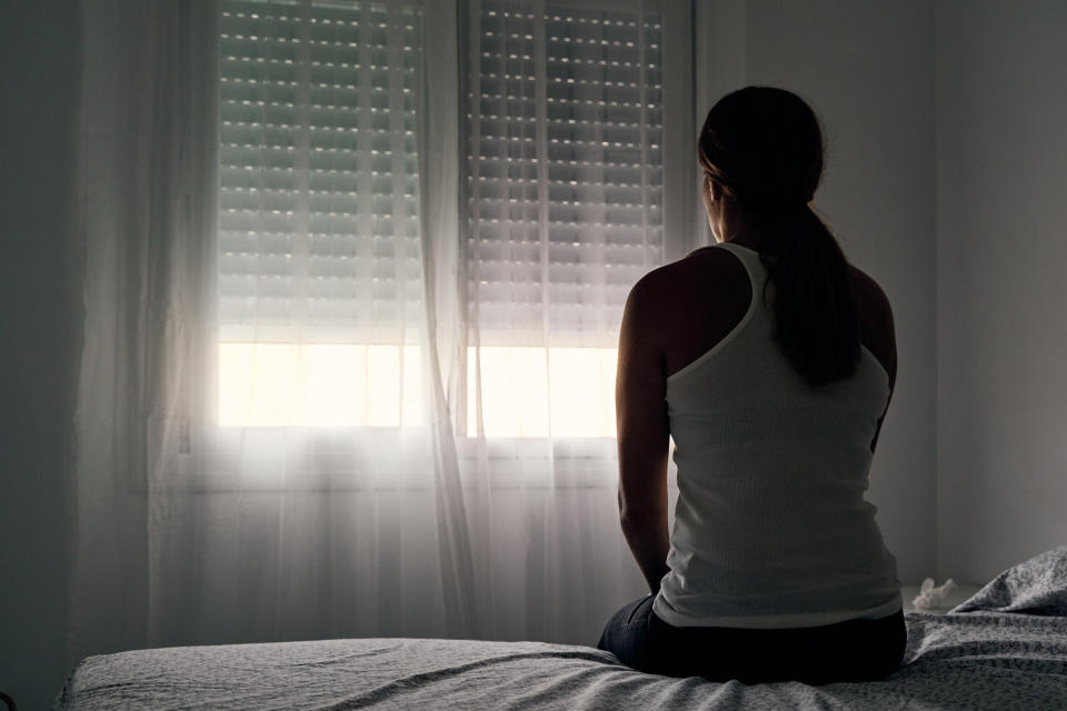 Someone sits alone in a dark bedroom