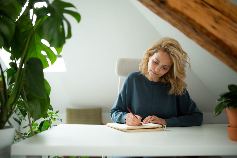 middle aged caucasian woman writing in a notepad at home