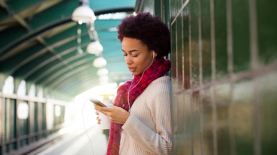 Young african woman at subway station waiting for the train and using mobile phone.