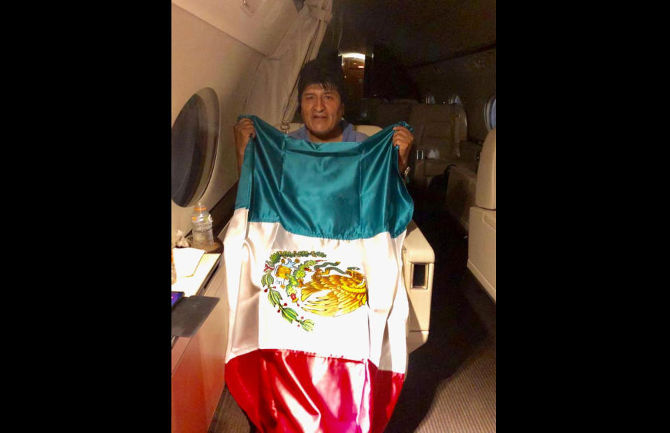This photo released by by Mexico's Foreign Minister Marcelo Ebrard shows Bolivia's former President Evo Morales holding a Mexican flag aboard a Mexican Air Force aircraft, Monday, Nov. 11, 2019. Morales has been granted asylum in Mexico after he resigned to the presidency on Nov. 10, under mounting pressure from the military and the public after a disputed re-election victory that triggered weeks of fraud allegations and deadly protests. (Mexico's Foreign Minister via AP)