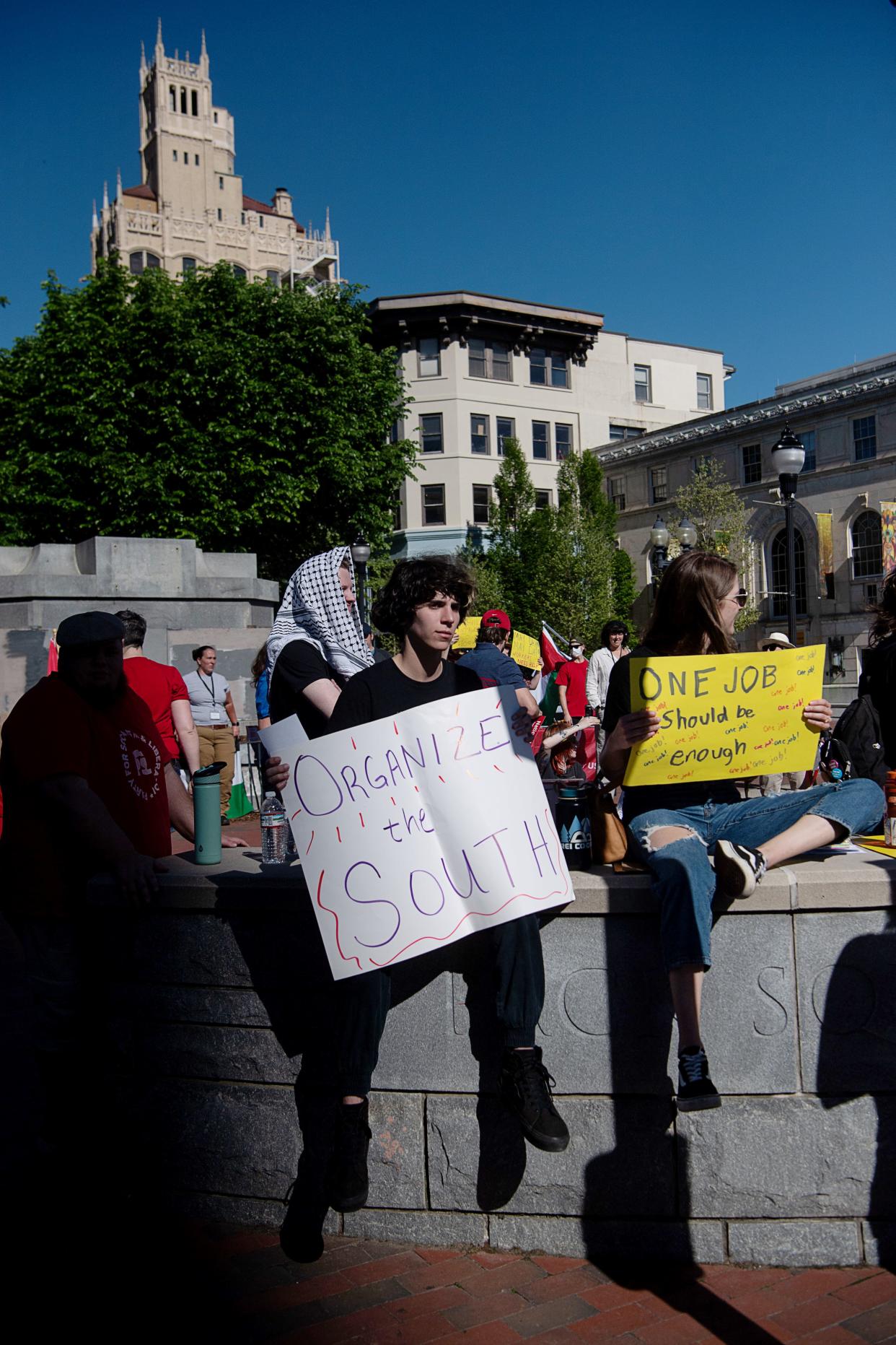 Attendees of a May Day rally hold signs in Pack Square as they listen to speakers, May 1, 2024.