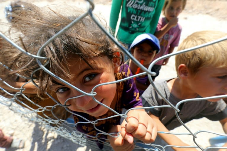 Displaced children from the Islamic State group's Syrian stronghold of Raqa pose for a photo behind a fence at a camp in Ain Issa on August 22, 2017