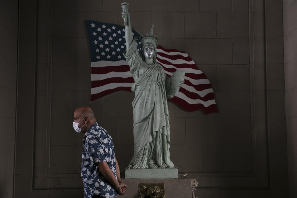 FILE - In this June 22, 2020, file photo, a man with a face mask walks past a replica of Statue of Liberty in Los Angeles. (AP Photo/Jae C. Hong, File)