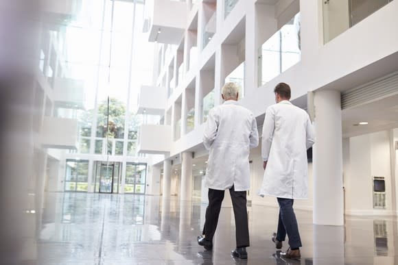 Two people in white lab coats walking through a hospital building atrium.