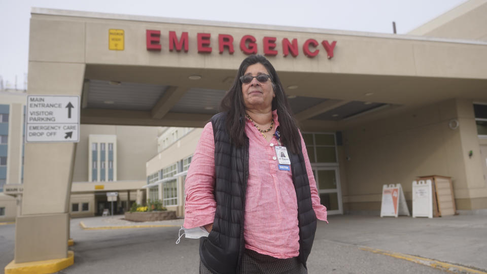 Angelique Ramirez, chief medical officer at Foundation Health Partners in Fairbanks, poses for a photograph in front of the emergency entrance at Fairbanks Memorial Hospital on Tuesday, Sept. 21, 2021, in Fairbanks, Alaska. Ramirez, said the facility has paused certain elective procedures, converted some meeting space for patient beds if needed and is hiring temporary non-licensed positions to take some duties off the hands of nurses, such as taking calls and stocking carts with personal protective gear. (AP Photo/Rick Bowmer)