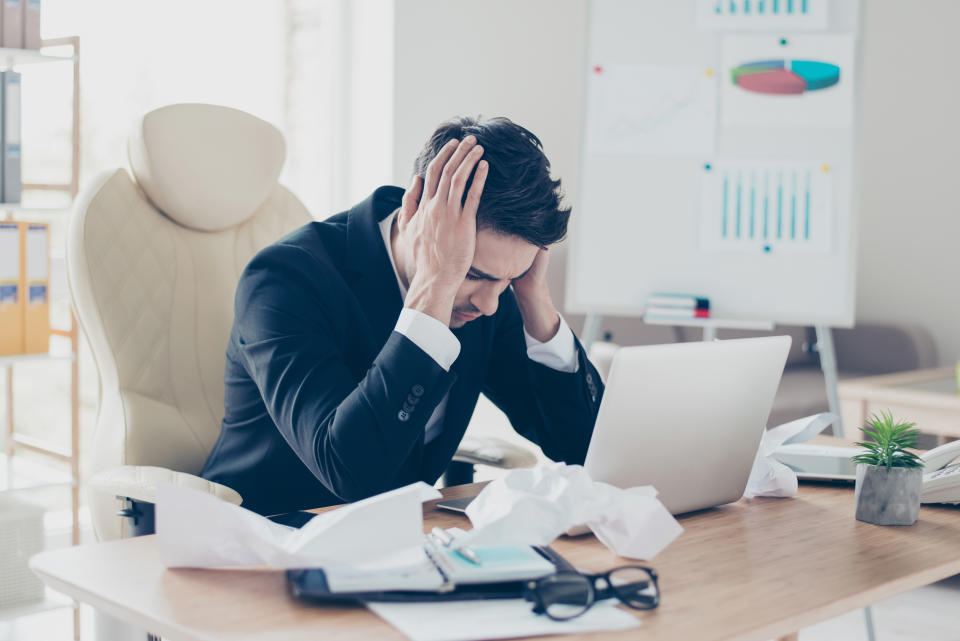 Portrait of exhausted sad nervous upset desperate marketer accountant freelancer holding head thinking about problems sitting at table with crumbled paper documents