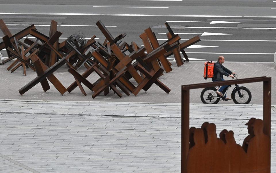 A delivery service employee rides a bycicle past past anti-tank hedgehogs in the center of the Ukrainian capital Kyiv on June 24, 2022 - Photo by SERGEI SUPINSKY/AFP via Getty Images