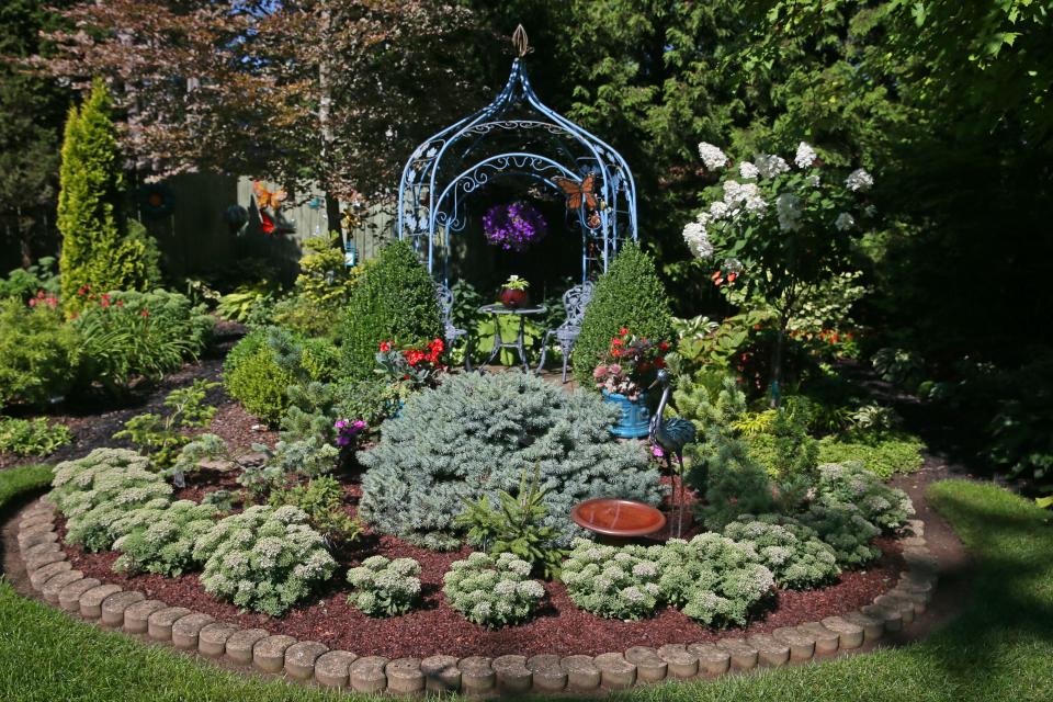 An ornate iron gazebo is the perfect spot to admire the flowers, plants and trees in the backyard garden of Dorothy Danforth.