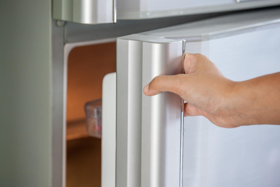 A hand opening a refrigerator door.
