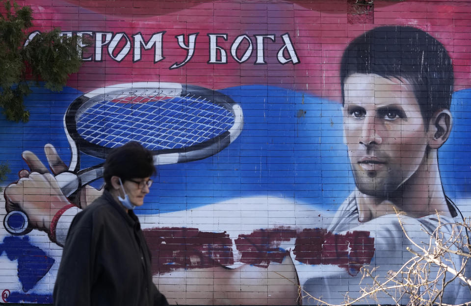 A woman passes a mural depicting Serbian tennis player Novak Djokovic, reading: "With faith in God" on a wall in Belgrade, Serbia, Sunday, Jan. 16, 2022. Novak Djokovic was preparing to leave Australia on Sunday evening after losing his final bid to avoid deportation and play in the Australian Open despite being unvaccinated for COVID-19. A court earlier unanimously dismissed the No. 1-ranked tennis player's challenge to cancel his visa. (AP Photo/Darko Vojinovic)