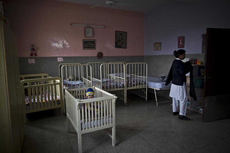 In this Saturday, Feb. 15, 2014, photo, Caleb, who just turned one year-old sits in a bed, while Pakistani nurse Farzana Yassmine, 31, arranges the children room, at St. Joseph’s Hospice, in Rawalpindi, Pakistan. Mohammed Aqeel spent weeks at home in Pakistan waiting for death after suffering a debilitating spinal cord injury in a car crash before friends suggested he come to St. Joseph’s Hospice on the outskirts of the capital, Islamabad. Now 13 years later, his life and those of some 40 others who live on its grounds might be changed forever as this hospital of last resort faces closure over its rising debts.(AP Photo/Muhammed Muheisen)