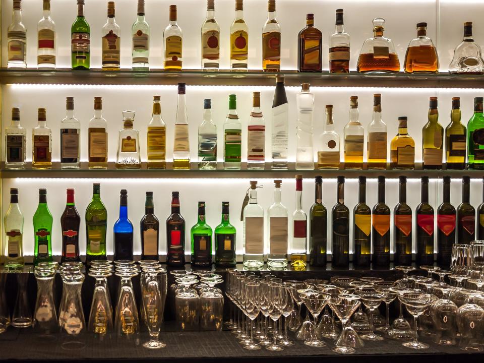 Bar of alcohol on shelves and several different kinds of cocktail glasses on the counter