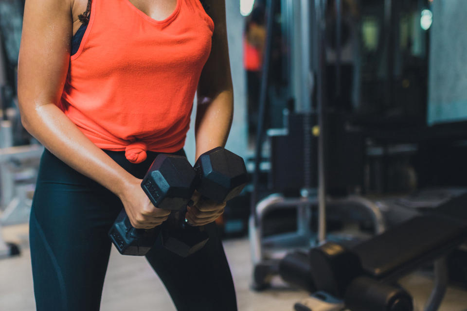 A person in gym attire holds two dumbbells in a fitness facility, ready to perform an exercise