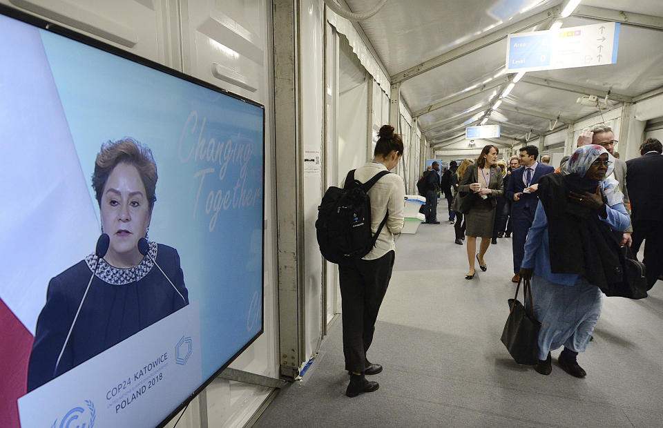 Participants in a U.N. climate conference walk by a screen showing high U.N. official for combatting climate change Patricia Espinoza, as she addresses the delegates in Katowice, Poland, Tuesday, Dec. 11, 2018. (AP Photo/Czarek Sokolowski)