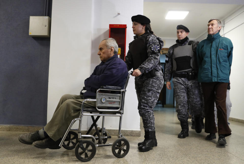 FILE - In this Aug. 5, 2019 file photo, Rev. Nicola Corradi, in wheelchair, and Rev. Horacio Corbacho, following behind in green, are escorted to a courtroom to attend their trial in Mendoza, Argentina. Judges are scheduled to rule Monday, Nov. 26, 2019, in the case of two priests who face up to 50 years in prison for alleged sexual abuse of deaf children at a Catholic-run school, a sister institution to a school that suffered a similar scandal in Italy. (AP Photo/Natacha Pisarenko, File)