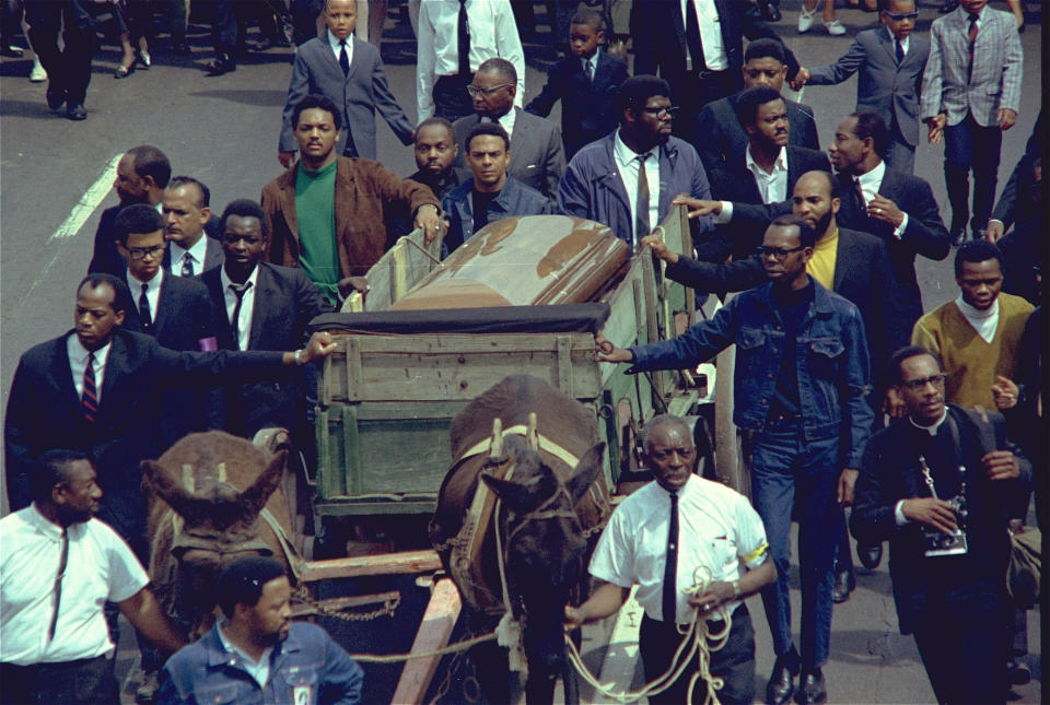 <p>A brace of plow mules draws the farm wagon bearing the mahogany casket of Dr. Martin Luther King Jr. Rev. Jesse Jackson, in green, and Andrew Young, at the left corner of the casket, are among the mourners. (Photo: AP) </p>