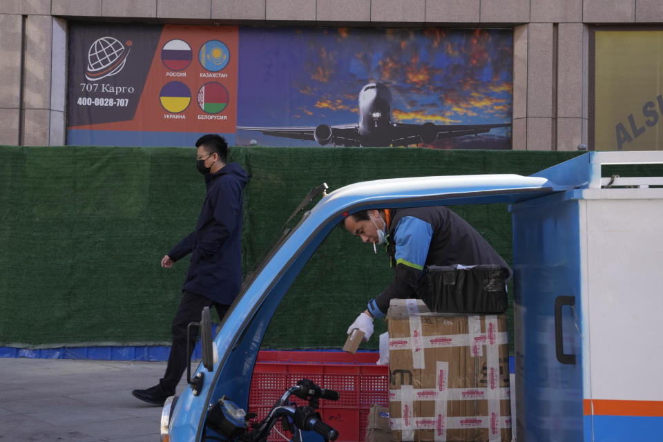 A delivery man prepares his packages as another man walks past an advertisement for cargo services to countries including Russia at a trading center on Saturday, Feb. 26, 2022, in Beijing. China is the only friend that might help Russia blunt the impact of economic sanctions over its invasion of Ukraine, but President Xi Jinping's government is giving no sign it might be willing to risk its own access to U.S. and European markets by doing too much. (AP Photo/Ng Han Guan)