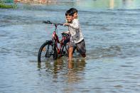 Children push a bicycle on a flooded street following heavy rains in Hyderabad on October 16, 2020. (Photo by NOAH SEELAM / AFP) (Photo by NOAH SEELAM/AFP via Getty Images)