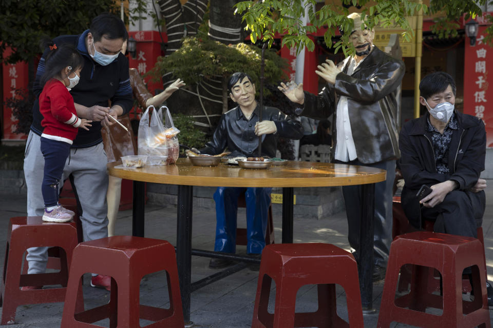 Residents wearing masks to help curb the spread the coronavirus rest among statues depicting normal life along a retail street in Wuhan, central China's Hubei province, Thursday, April 9, 2020. Released from their apartments after a 2 1/2-month quarantine, residents of the city where the coronavirus pandemic began are cautiously returning to shopping and strolling in the street but say they still go out little and keep children home while they wait for schools to reopen. (AP Photo/Ng Han Guan)