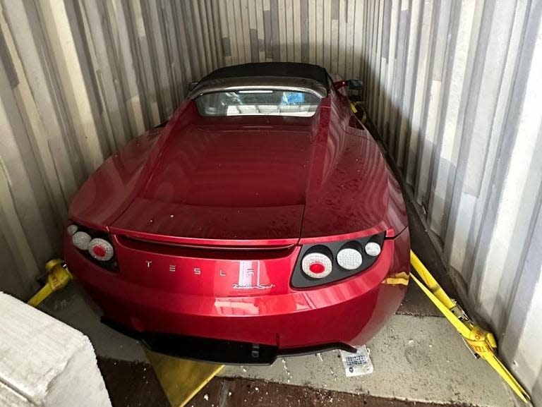 A red 2010 Tesla Roadster in a shipping container.