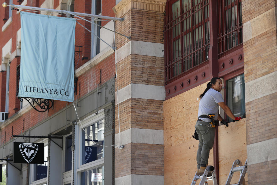 A worker installs boards over the windows of a Tiffany's store Sunday, May 31, 2020, in the SoHo neighborhood of New York, which was vandalized during protests Saturday night over the death of George Floyd. Floyd died Monday after he was pinned at the neck by a Minneapolis police officer. (AP Photo/Kathy Willens)