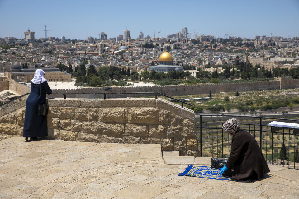A Muslim woman wears gloves prays in east Jerusalem's Mount of Olives, overlooking the Dome of the Rock and al-Aqsa mosque compound, which remains shut to prevent the spread of coronavirus during the holy month of Ramadan, Friday, May 1, 2020. (AP Photo/Ariel Schalit)