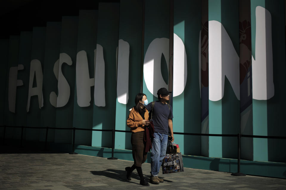 A couple with their purchased goods walk through the capital city's popular shopping mall in Beijing, Monday, Oct. 19, 2020. China’s shaky economic recovery from the coronavirus pandemic is gaining strength as consumers return to shopping malls and auto dealerships while the United States and Europe endure painful contractions.(AP Photo/Andy Wong)