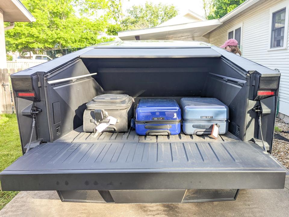 Tesla Cybertruck bed with the tailgate down and cover up, with suitcases inside.