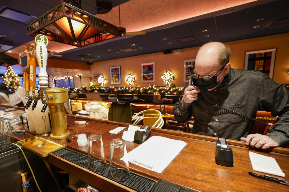 Steve Olsen, the owner of the West Bank Café, reads the specials over the phone to a to-go customer in the empty restaurant, Saturday, Jan. 9, 2021, in the Hell's Kitchen neighborhood of New York. The boarded-up windows and For Rent signs are all over the place in Manhattan’s Hell’s Kitchen neighborhood. Nearby, the Broadway theaters are all dark. But the economic darkness brought on by the coronavirus pandemic has had a few bright spots. A couple of well-loved venues have gotten financial boosts, thanks to online fundraising campaigns and even a telethon. (AP Photo/Mary Altaffer)