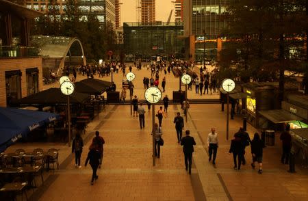 People walk through Canary Wharf while the sky overhead turns red as dust from the Sahara carried by storm Ophelia filters sunlight over London, Britain, October 16, 2017. REUTERS/Tom Jacobs