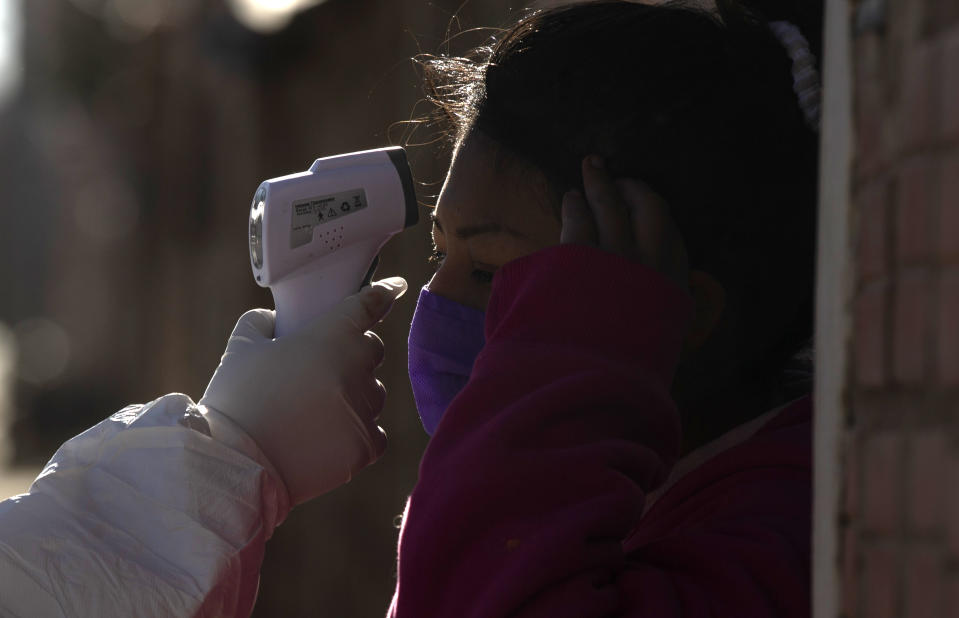 A doctor measures the temperature of woman during a house-to-house new coronavirus testing campaign in the Villa Jaime Paz Zamora neighborhood of El Alto, Bolivia, Saturday, July 4, 2020. (AP Photo/Juan Karita)