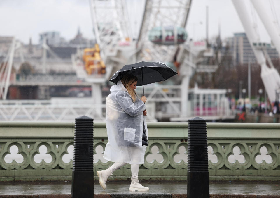A pedestrian wearing a raincoat carries an umbrella as she crosses Westminster Bridge, in London, Britain, February 22, 2024, as Met Office issues fresh yellow rain warning for capital. REUTERS/Isabel Infantes