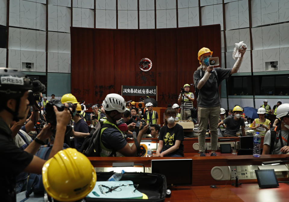 FILE - In this July 1, 2019, file photo, a protester talks to others in front of a defaced Hong Kong logo after breaking in at the Legislative Chamber to protest against the extradition bill in Hong Kong. From across the political spectrum, Hong Kong residents condemned mob violence at the U.S. Capitol, 18 months after they saw protesters storm their own local legislature. (AP Photo/Vincent Yu, File)