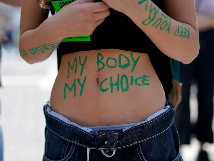 A person's bare stomach bears the words &quot;my body my choice&quot; in green paint.