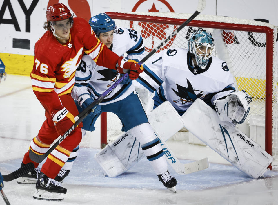 San Jose Sharks defenseman Calen Addison (33) checks Calgary Flames forward Martin Pospisil (76) as goalie Devin Cooley (1) follows the play during the second period of an NHL hockey game Thursday, April 18, 2024, in Calgary, Alberta. (Jeff McIntosh/The Canadian Press via AP)