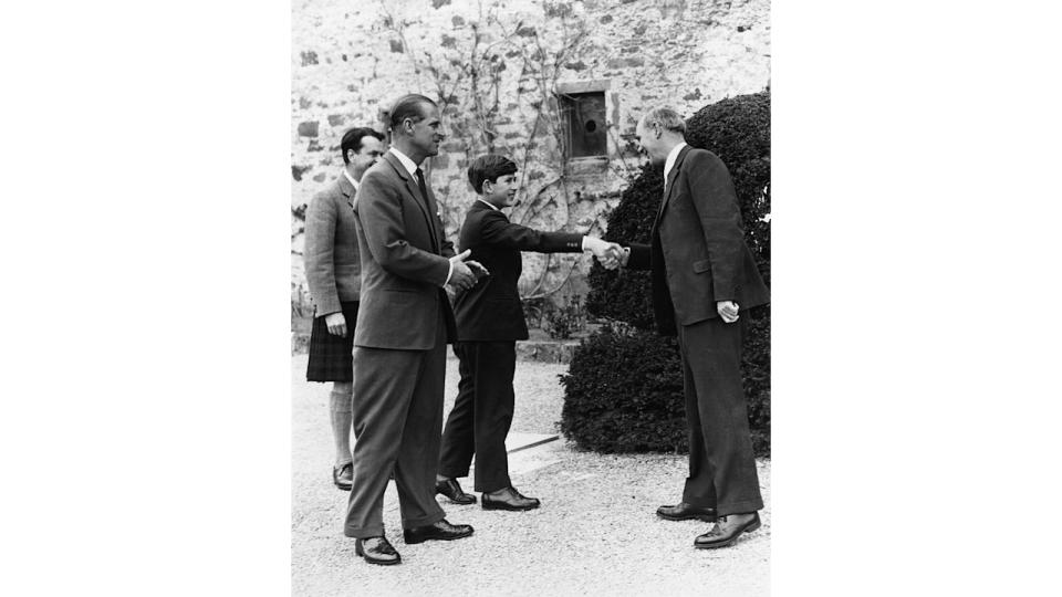 King Charles shaking hands with a headmaster with Prince Philip by his side