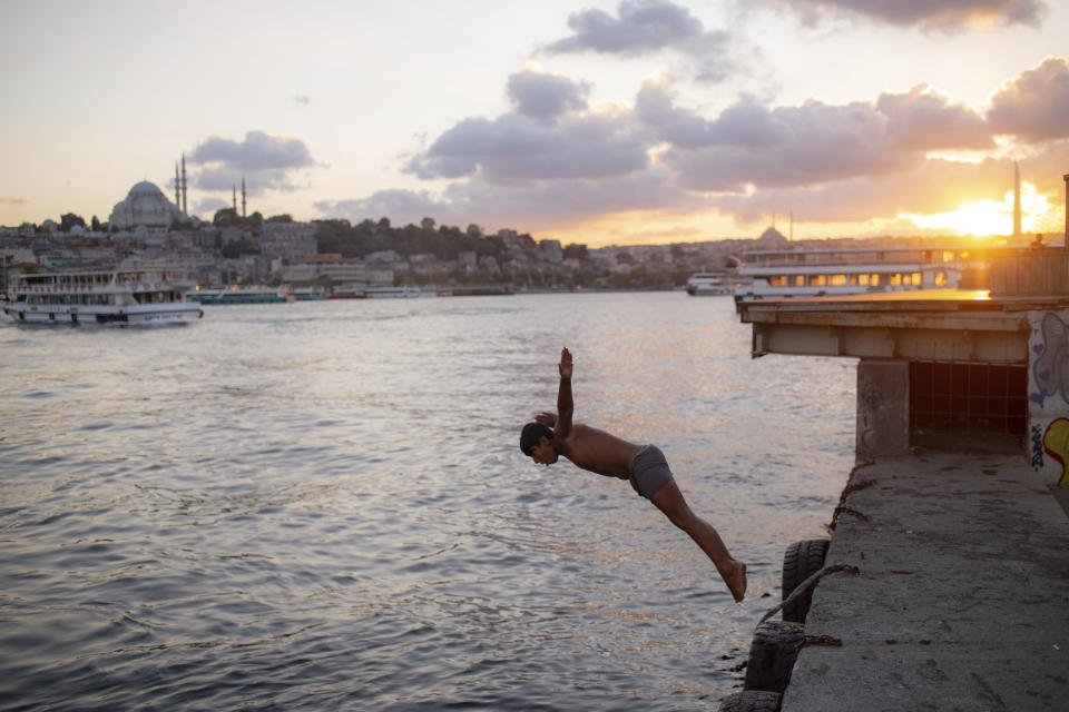 A youth jumps into the Golden Horn in Istanbul, Friday, Sept. 11, 2020. Turkey is getting tough on people who flout self-isolation rules despite testing positive for the coronavirus. An Interior Ministry circular sent to the country's 81 provinces on Friday said people caught leaving their homes despite isolation orders will be quarantined and supervised at state-owned dormitories or hostels. (AP Photo/Yasin Akgul)