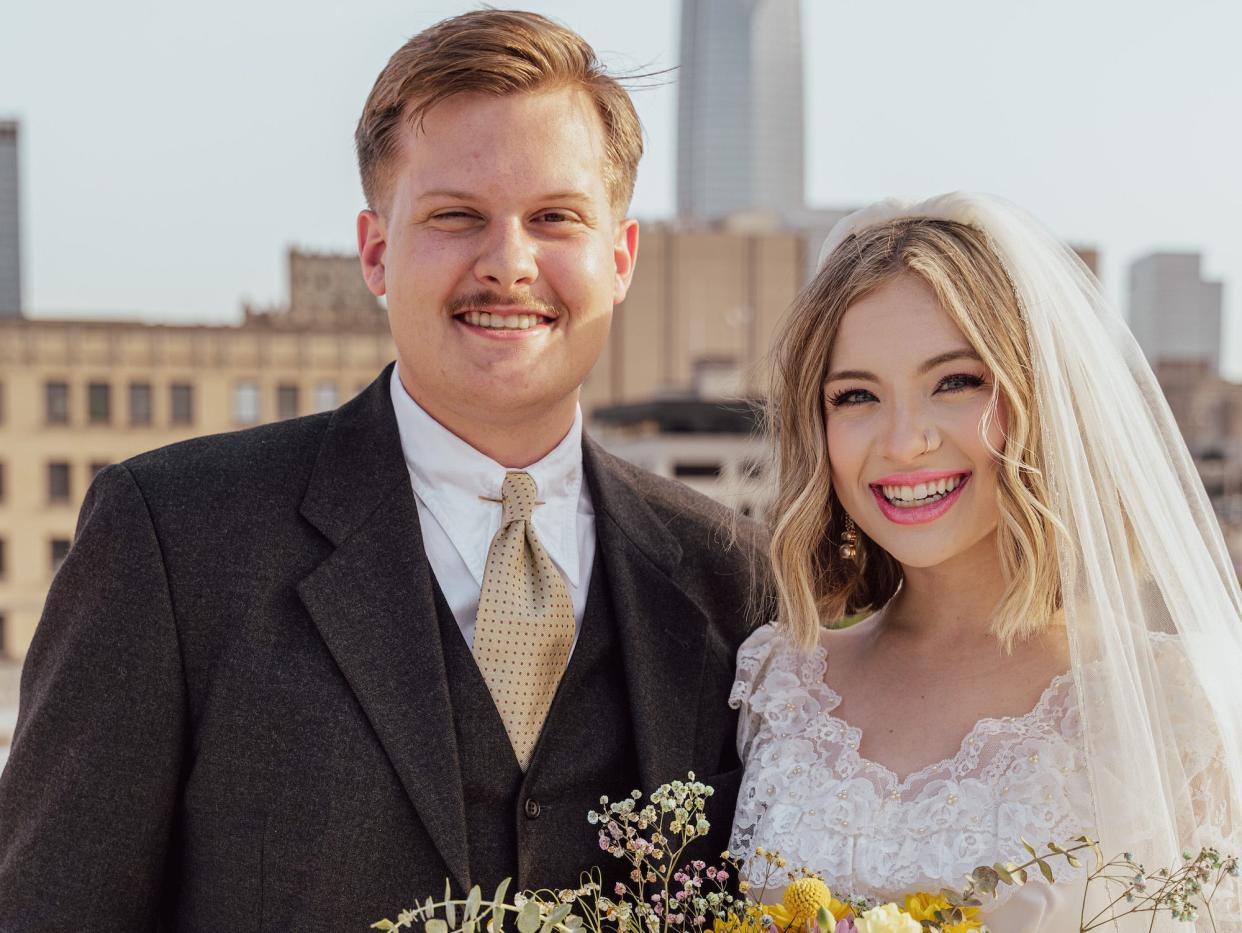 A bride and groom smile on their wedding day as she holds a bouquet of flowers.