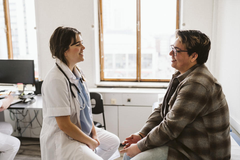 Doctor in white coat smiling at patient seated in office, promoting a healthy doctor-patient relationship