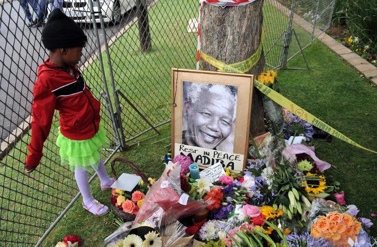 A young girl looks at a portrait of South African former President Nelson Mandela on December 6, 2013 outside his house in Johannesburg