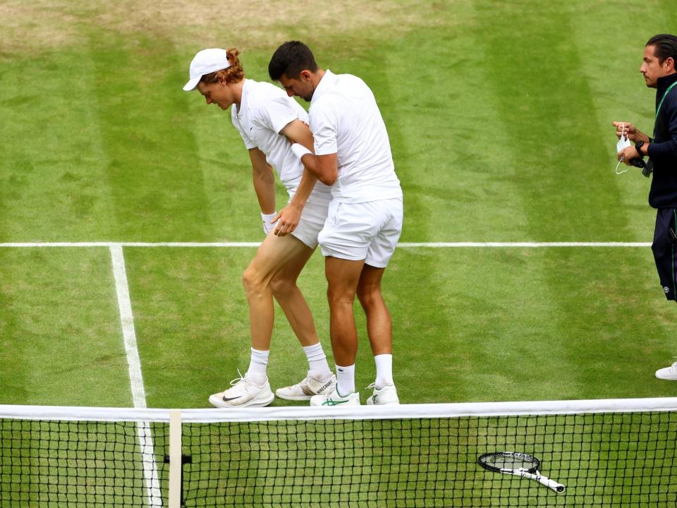 Novak Djokovic helps Jannik Sinner to his feet at Wimbledon.