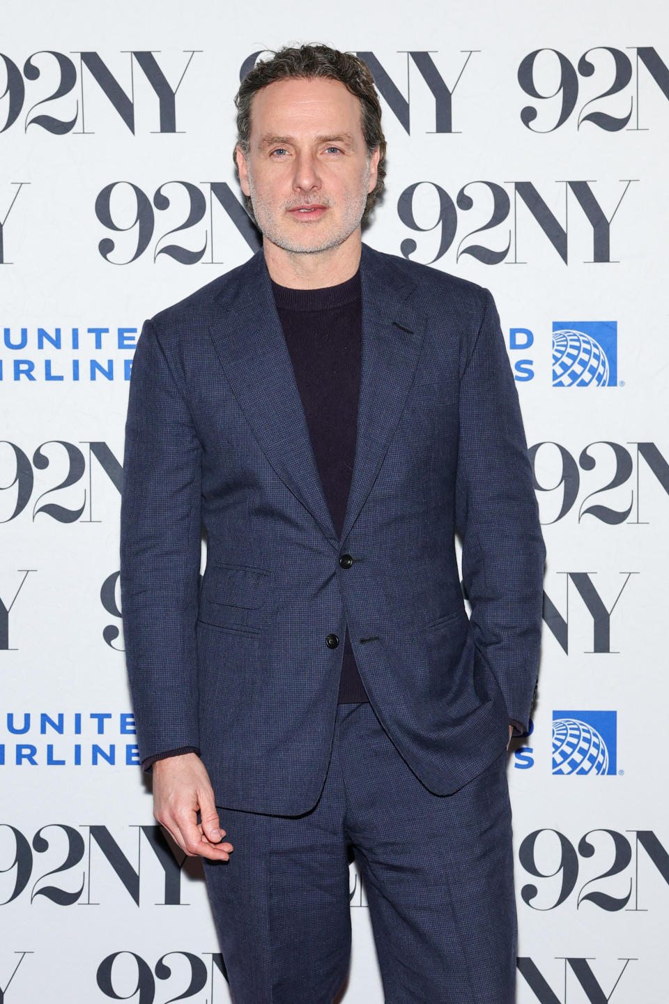 Andrew Lincoln in a blue suit poses on the red carpet at a 92NY event