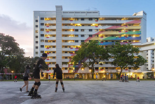 A group of rollerbladers before a public HDB residential block in Hougang, with a large mural of a rainbow painted across its facade.