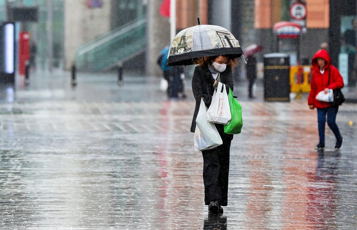 A shopper walks through the rain with an umbrella after a change in the weather has seen the mini heatwave come to an end: PA