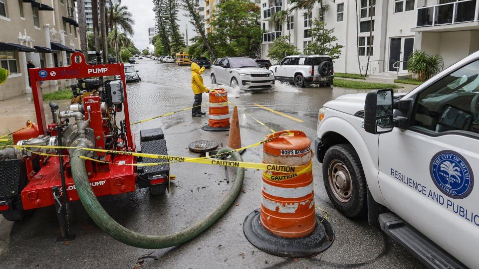 A City of Miami Public Works employee waves towards a vehicle driving through a flooded street in Edgewater along N.E. 23rd Street in Miami, on Wednesday, June 12, 2024. (Al Diaz/Miami Herald via AP)