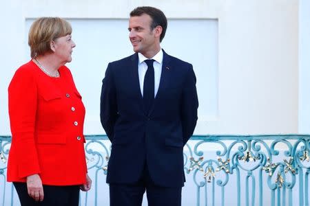 German Chancellor Angela Merkel and French President Emmanuel Macron react as they await European Commission President Jean-Claude Juncker in Meseberg, Germany, June 19, 2018. REUTERS/Hannibal Hanschke